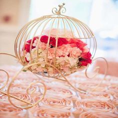 a birdcage filled with pink and red flowers on top of a table covered in roses