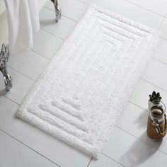 a white bath mat sitting on top of a bathroom floor next to a potted plant