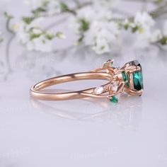 an emerald and diamond ring on a white surface with flowers in the backgroud