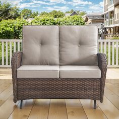 a wicker couch sitting on top of a wooden floor next to a white fence