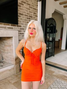 a woman in an orange dress standing next to a fire place with her hands on her hips