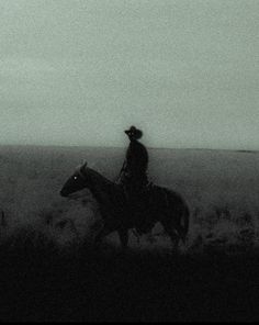 black and white photograph of man on horse in open field with distant area behind him