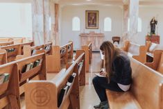 a woman sitting on top of a wooden bench in a room filled with pews