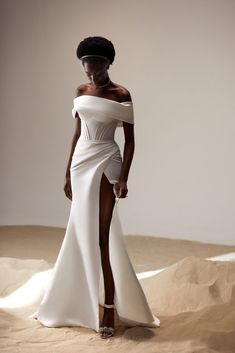 a woman in a white dress and headpiece standing on sand dunes with her legs crossed