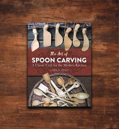 the art of spoon carving book on a wooden table with utensils and spoons