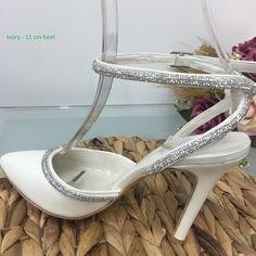 a pair of white high heeled shoes sitting on top of a woven basket next to flowers