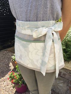 a woman in grey shirt and gray pants wearing an apron with flowers on it's waist