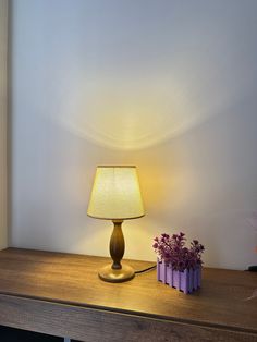 a table with a lamp on it next to a flower pot and a purple container