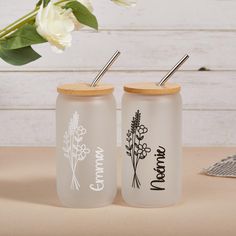 two personalized glass tumblers with straws and flowers on the lids, one is empty