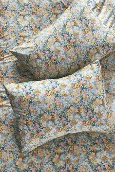 three pillows sitting on top of a bed covered in floral print sheets and pillow cases