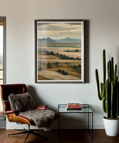 a painting hangs on the wall next to a chair and table with a cactus in it