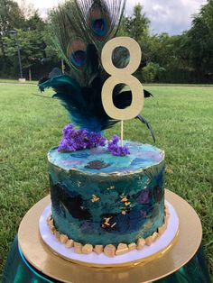 there is a cake that has been decorated with peacock feathers and purple flowers on it