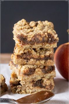 three granola bars stacked on top of each other with an apple in the background