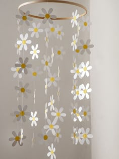 a white and yellow mobile with flowers hanging from it's center circle, in front of a gray wall