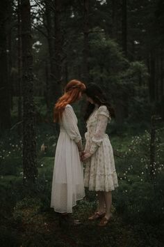 two women in white dresses standing next to each other holding hands and looking at each other