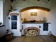 an old fashioned kitchen with wood burning in the oven and logs stacked on the floor