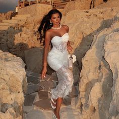 a woman in a white dress walking on rocks