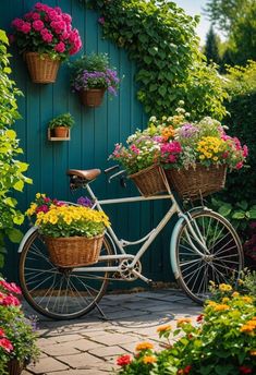 a bicycle with baskets full of flowers parked in front of a green wall filled with potted plants