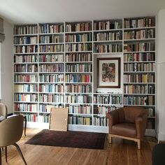 a living room filled with lots of books on top of a book shelf next to a chair