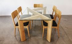 a glass dining table with wooden chairs and a black cushion on the backrests