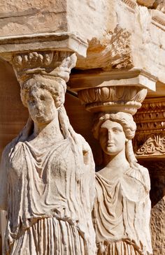 two statues are standing next to each other on the side of a stone building, one is holding a planter