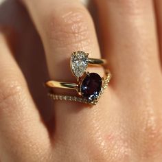 a woman's hand with two rings on top of her finger, and an oval shaped diamond in the middle