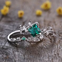 a ring with an emerald colored stone in the center and vines around it on top of a wooden surface