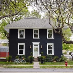 a black house with white windows and a bicycle parked in the front yard next to it