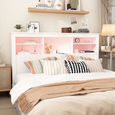 a white bed topped with lots of pillows next to a shelf filled with pictures and books