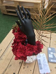 a vase filled with red flowers on top of a wooden table next to a phone