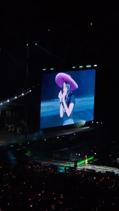 a large screen with a woman on it in the middle of an arena at night