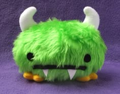 a green stuffed animal with large horns and big fangs on it's face, sitting on a purple surface