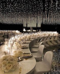 a long table with white chairs and flowers on it is surrounded by chandeliers