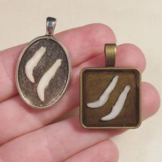 a hand holding a small pendant with two white objects on it's back side