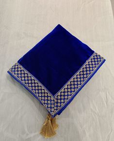 a blue and gold square pillow with tassels on the end sitting on a white sheet