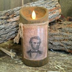 a candle that is sitting on the ground next to some logs and wood chips with a picture of abraham lincoln printed on it