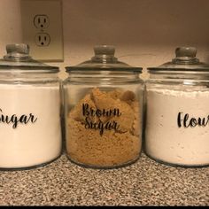 three glass jars with brown sugar and flour in them sitting on a counter next to a light switch