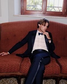 a young man in a tuxedo sitting on a couch with his legs crossed