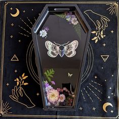 a decorative display case with flowers and butterflies on the front, sitting on a black table cloth