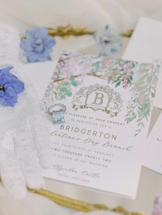 the wedding stationery is laid out on top of the bed with blue flowers and gold trimmings