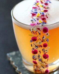 a glass filled with liquid and flowers on top of a metal tray next to a spoon