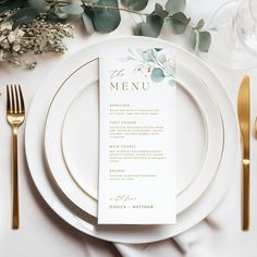 a place setting with white plates, gold cutlery and greenery on the table