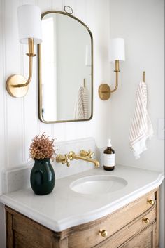 a bathroom sink with a green vase on it and a gold mirror above the sink