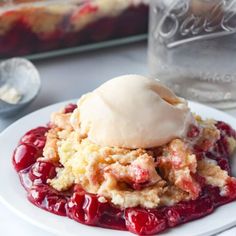 a white plate topped with fruit cobbler next to a glass of water and ice cream