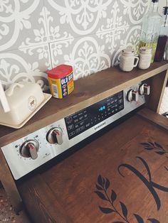 a stove top oven sitting on top of a wooden counter next to a wall paper