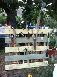 a garden tool rack made out of pallets and wooden planks with gardening tools hanging on it