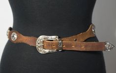 Here is a brown leather belt with silver tone metal concho embellishments and a southwestern pattern with a silver color metal buckle. You'll love its rodeo ranch style. And you'll love pairing it with your favorite western jeans, denim dresses or skirts. This belt is in overall good condition with signs of wearing; scuffing and use and it's very collectible with the DUN DEE brand stamp that's made in Texas, USA. It's stamped a size 32. Check out photos for this belt and check out its measuremen Southwestern Concho Belt For Western-themed Events, Southwestern Style Concho Belt For Festivals, Western Brown Belt With Concho, Southwestern Style Brown Concho Belt, Vintage Brown Belt For Western-themed Events, Western Style Brown Concho Belt, Western Brown Belt Buckles With Silver Buckle, Rustic Concho Belts For Rodeo, Southwestern Leather Belt Buckles For Western-themed Events