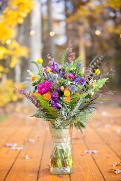 a vase filled with lots of flowers on top of a wooden table next to trees