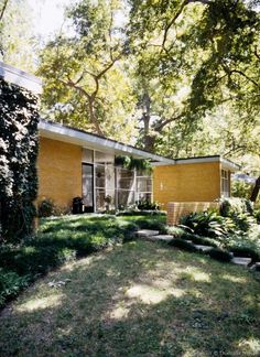 a yellow brick house sitting in the middle of a lush green yard with lots of trees