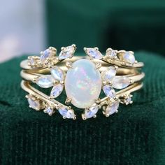 an opal and diamond ring sits on top of a green cloth